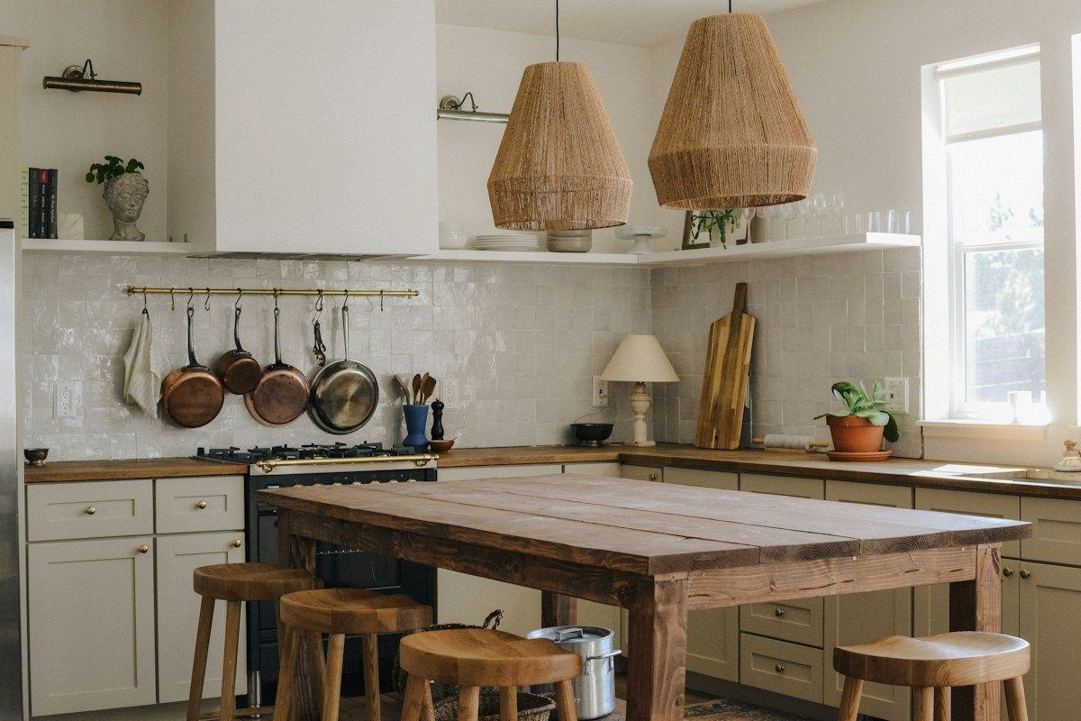 A bright white kitchen with woven pendant lights and a wood island